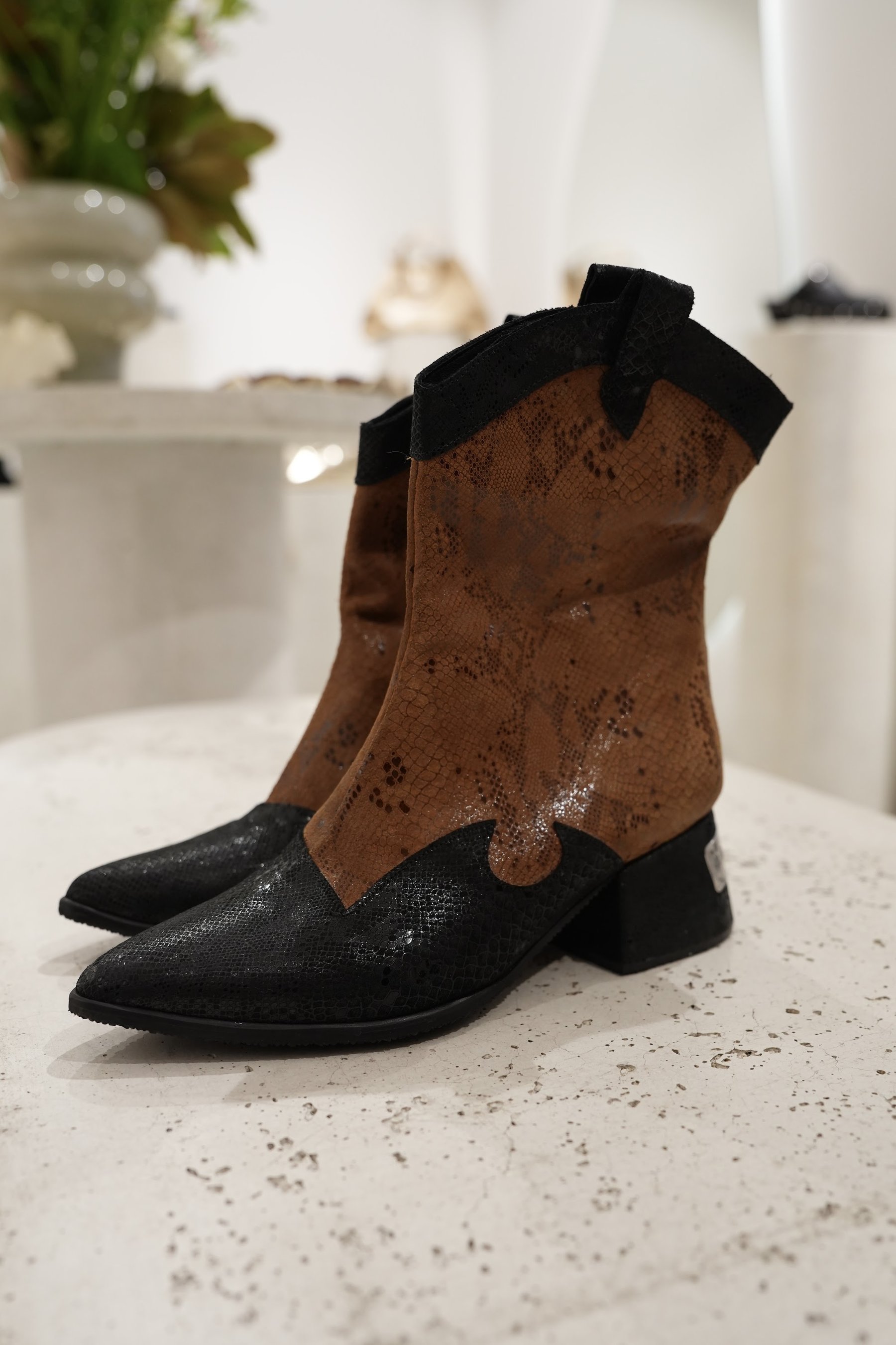 Bota de gamuza café y botín negro sobre la repisa de exhibición.