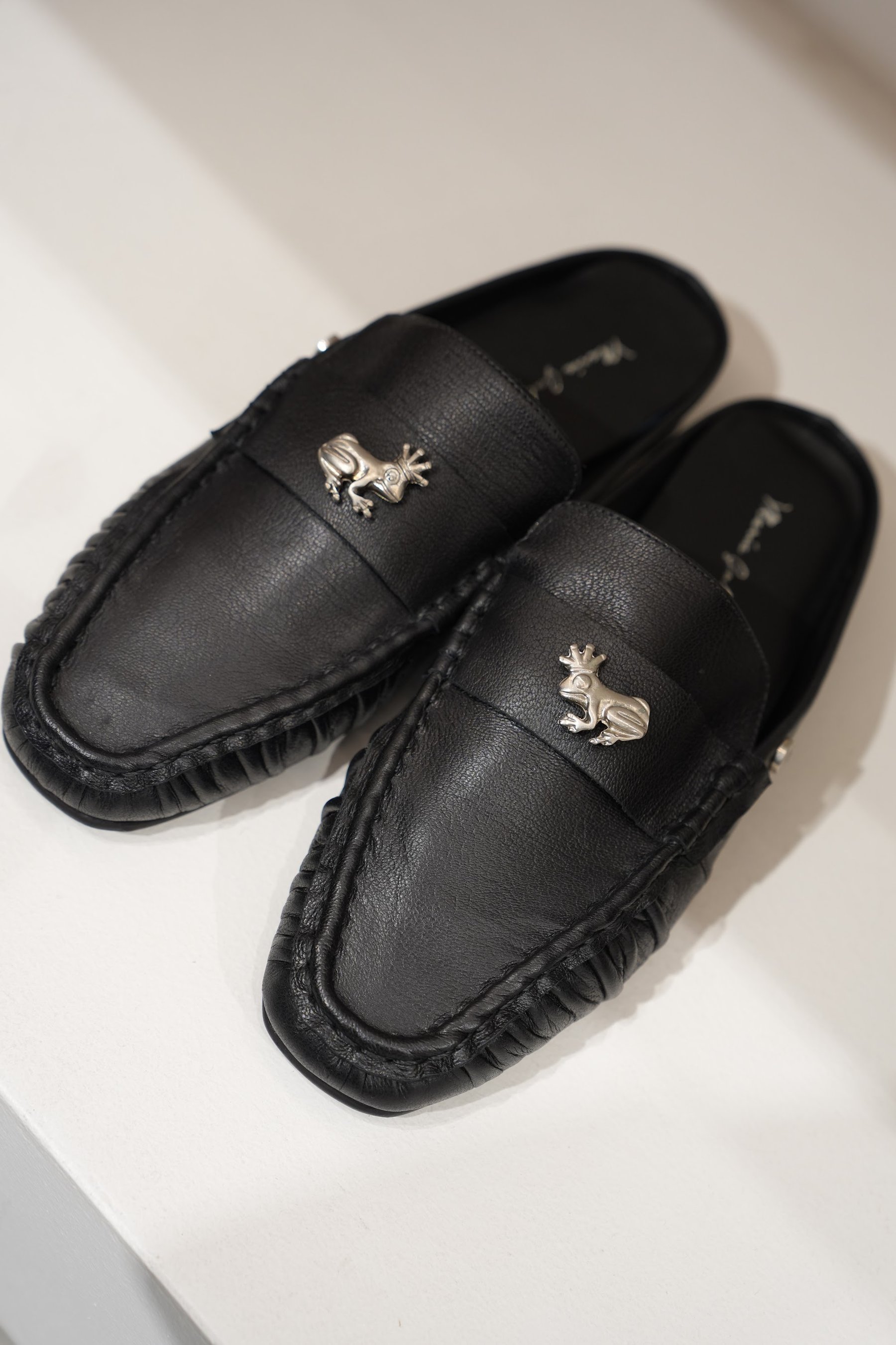 Par de mocasines negros con herraje sobre superficie blanca.