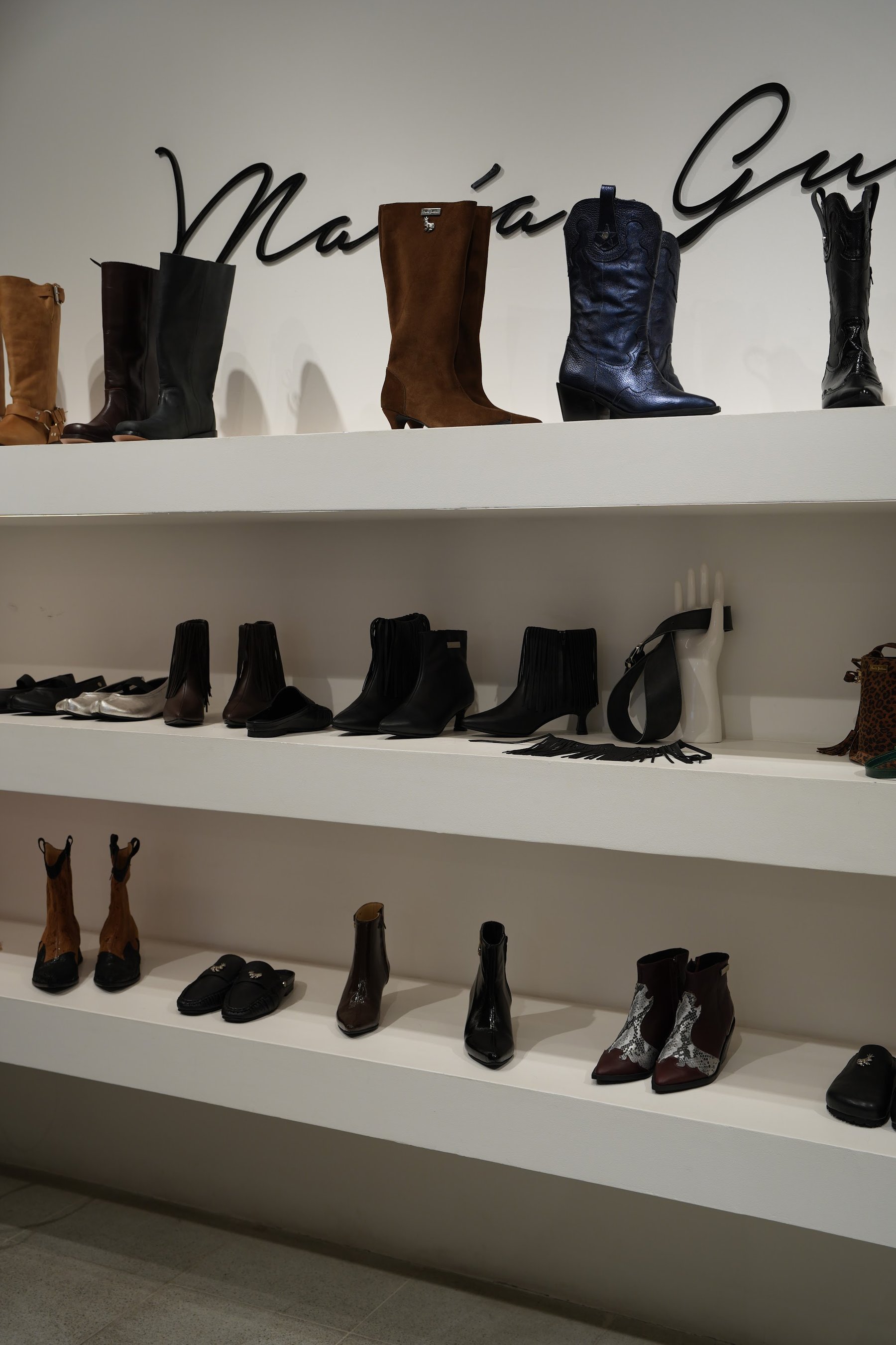 Repisas con botas altas y botines alineados bajo el logotipo de la marca.