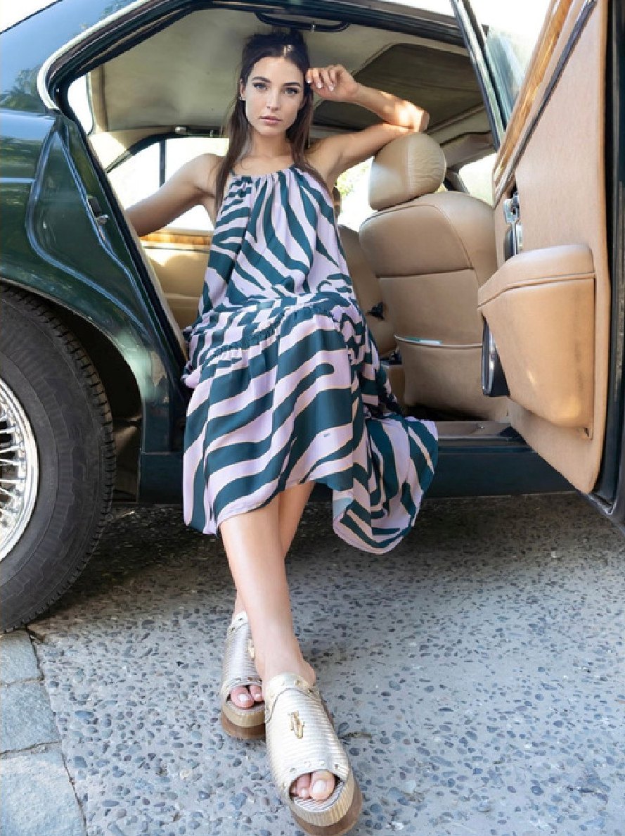 Modelo con vestido de rayas apoyada en la puerta abierta de un auto.