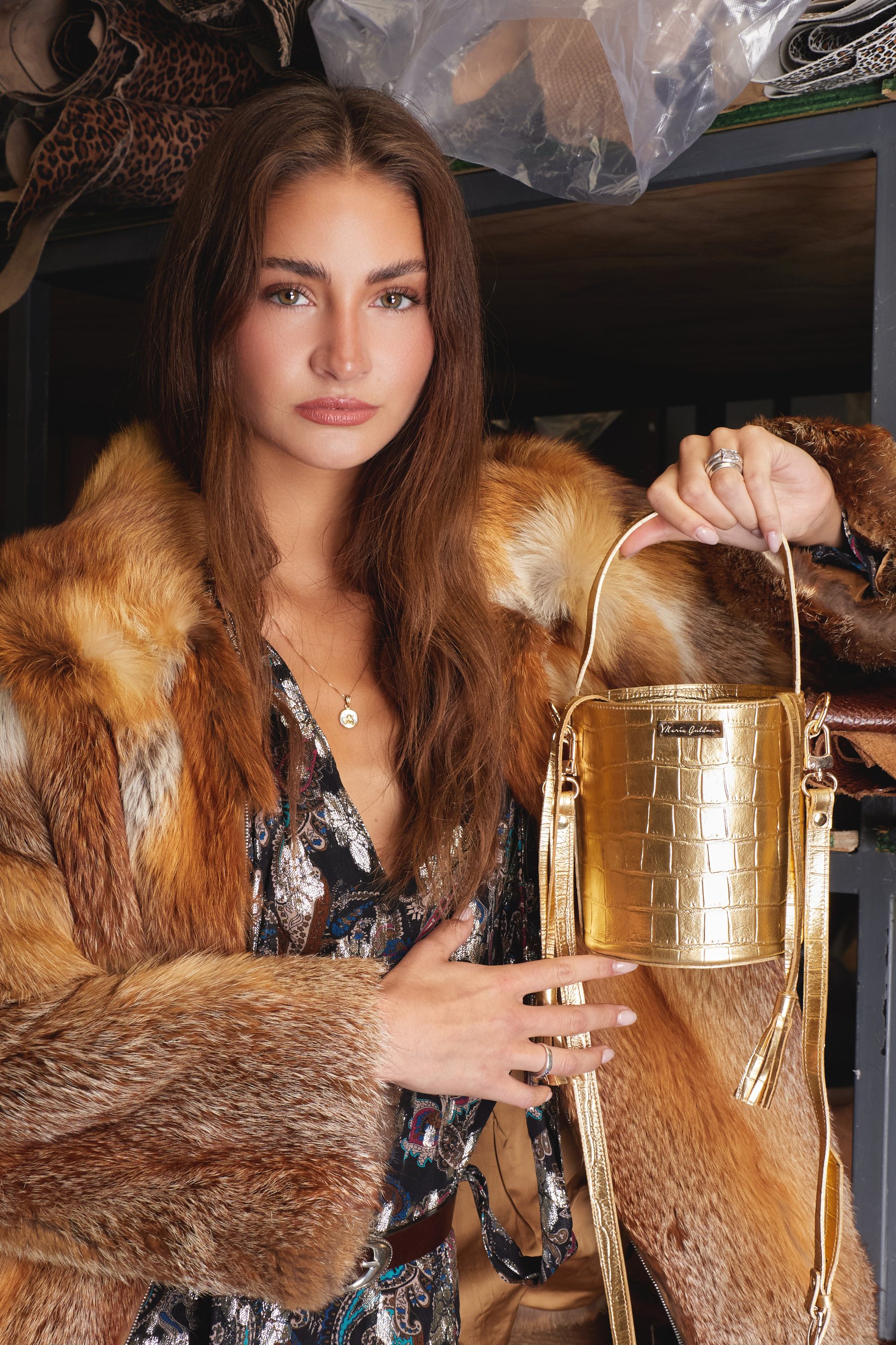 Editorial El Encargo — modelo con abrigo de piel y bolso bucket dorado, fotografiada en una curtiduría.