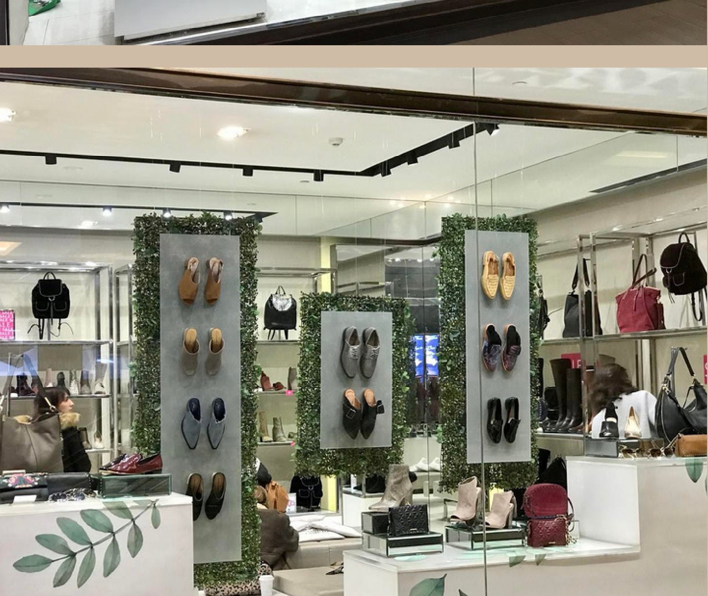 Interior de la tienda con paneles de follaje y exhibición de calzado y bolsos.
