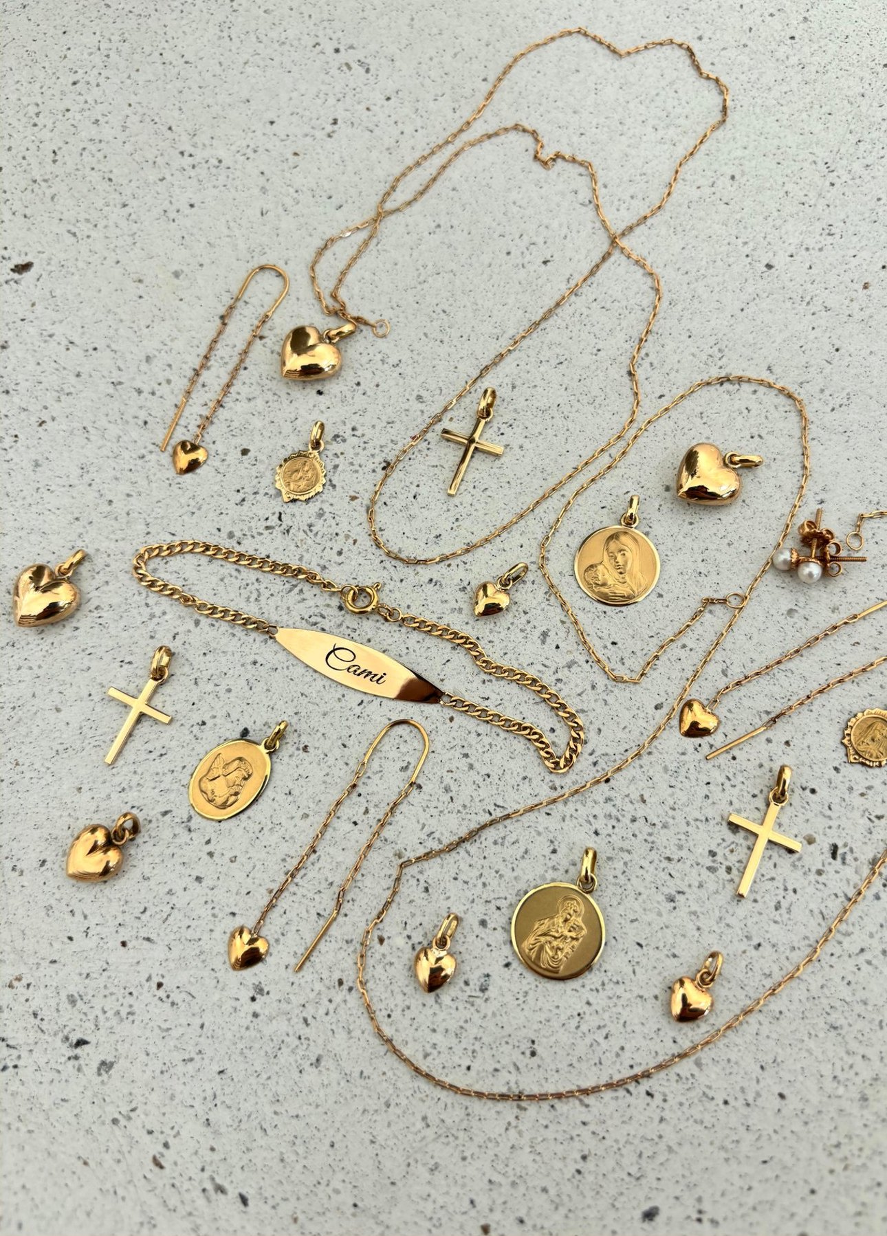 Piezas de joyería en oro 18K dispuestas sobre una superficie de terrazo.