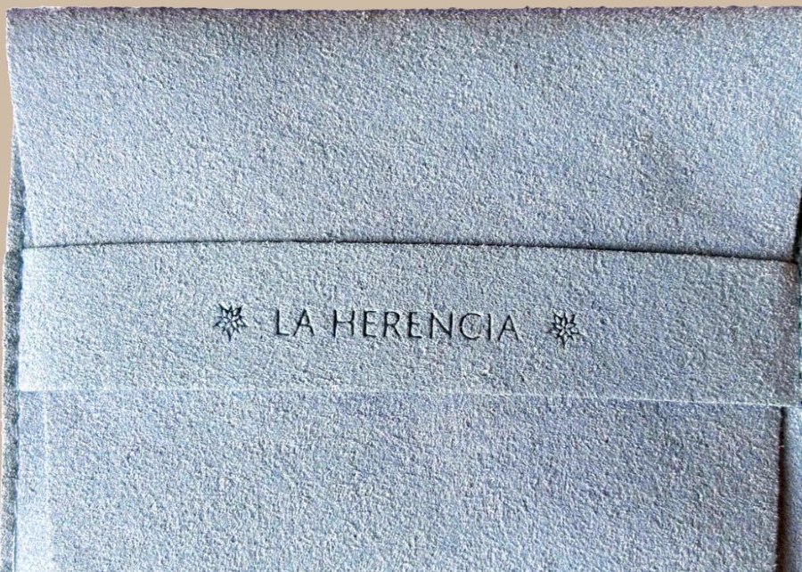 Sobre de tela gris con solapa interna y logotipo.