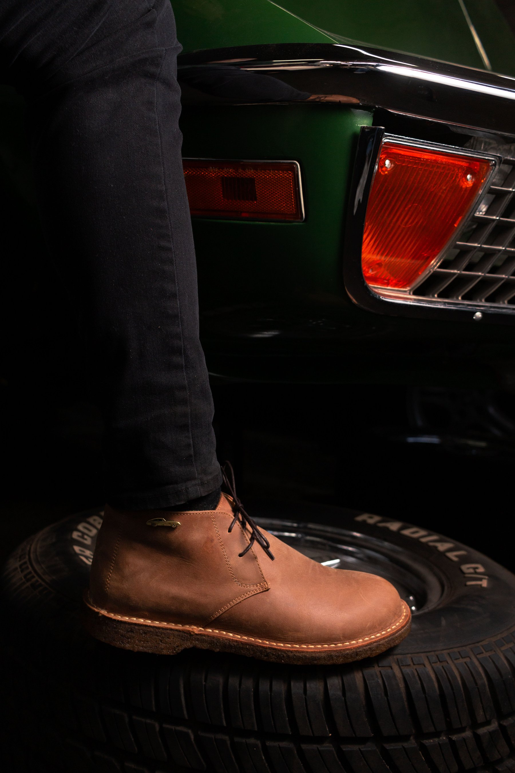 Pie calzado con la bota apoyado en el neumático de un auto verde.