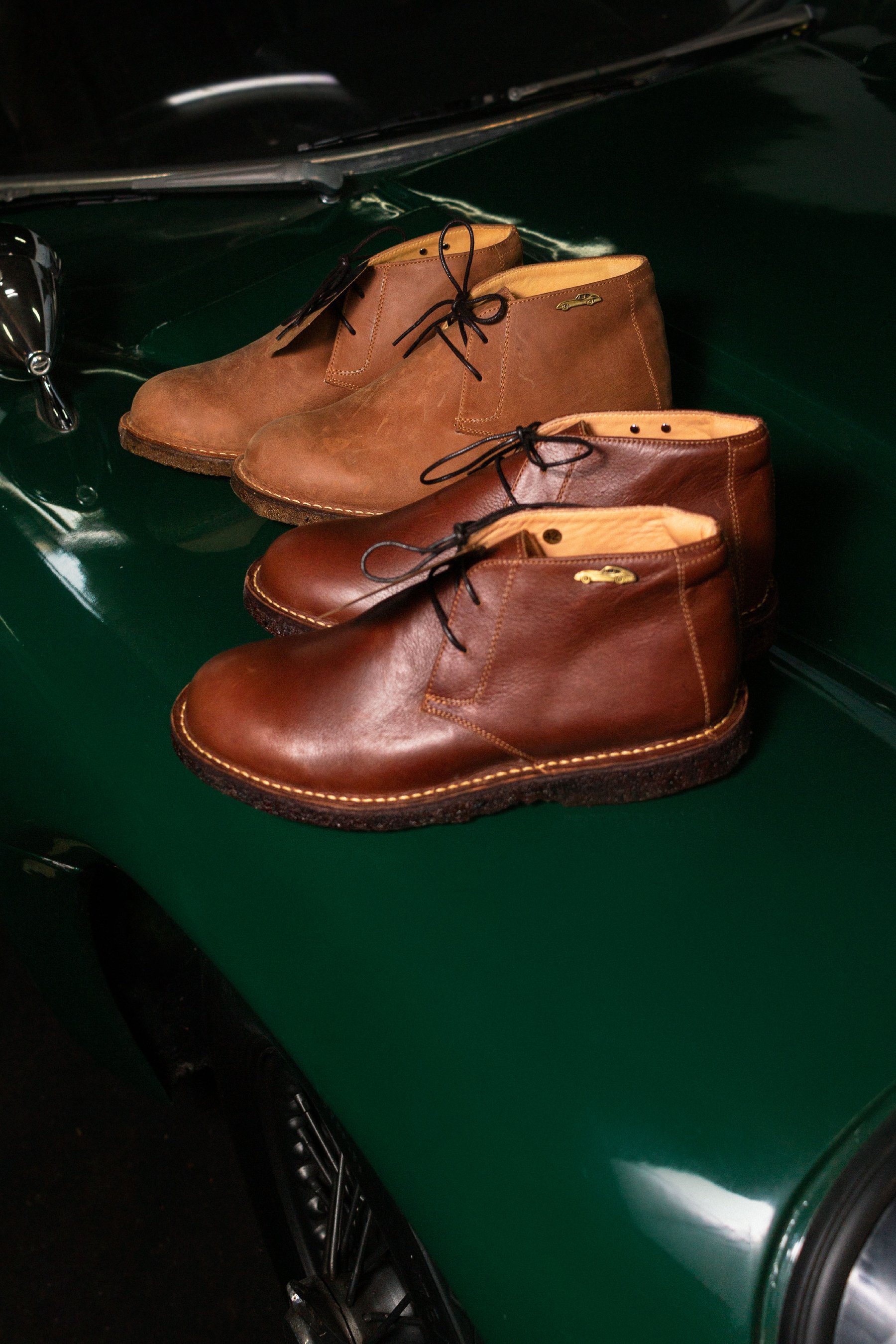 Botas de cuero café sobre la carrocería verde de un auto clásico.
