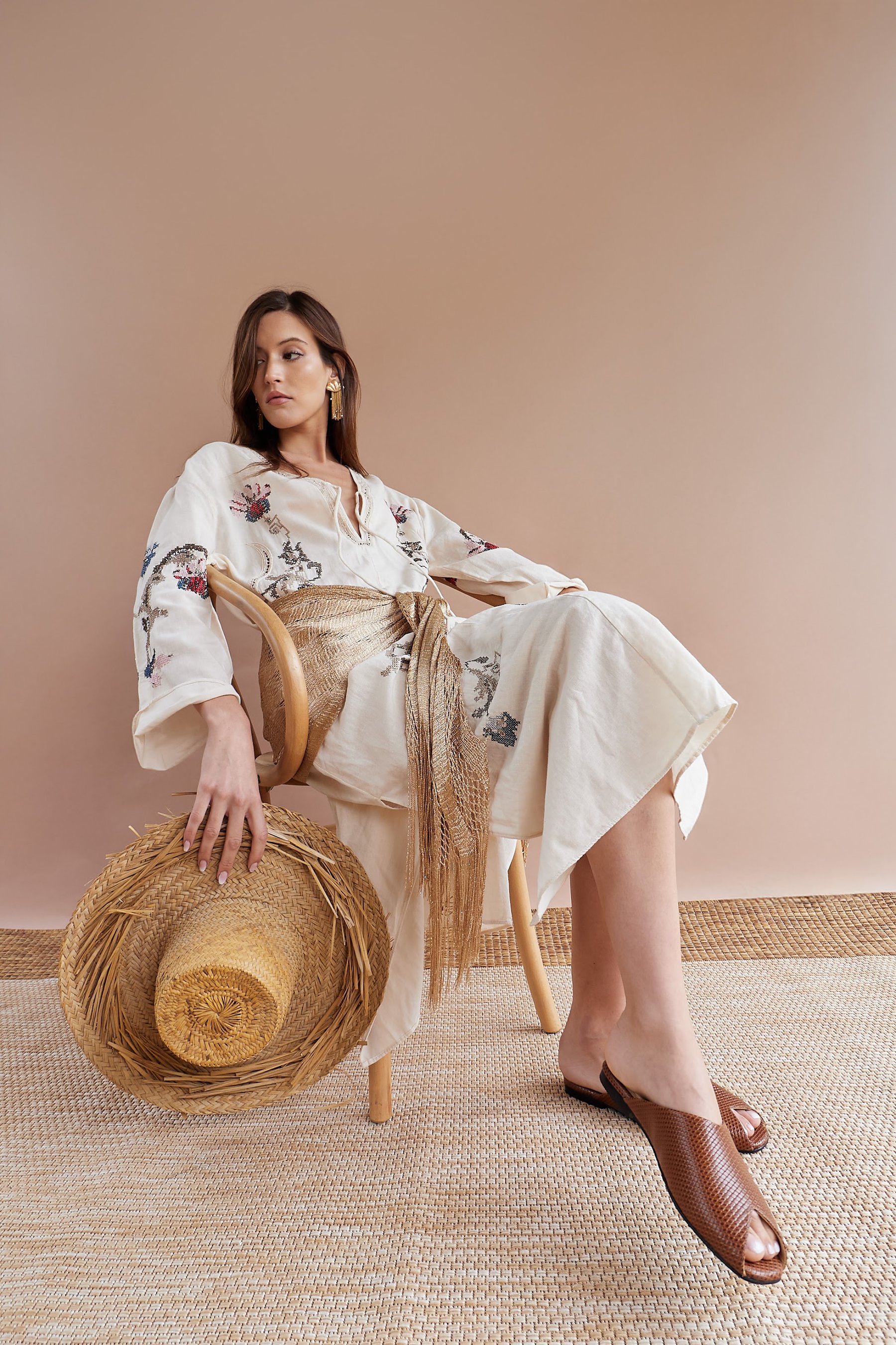 Modelo con conjunto bordado crudo y sombrero de paja junto a la silla.
