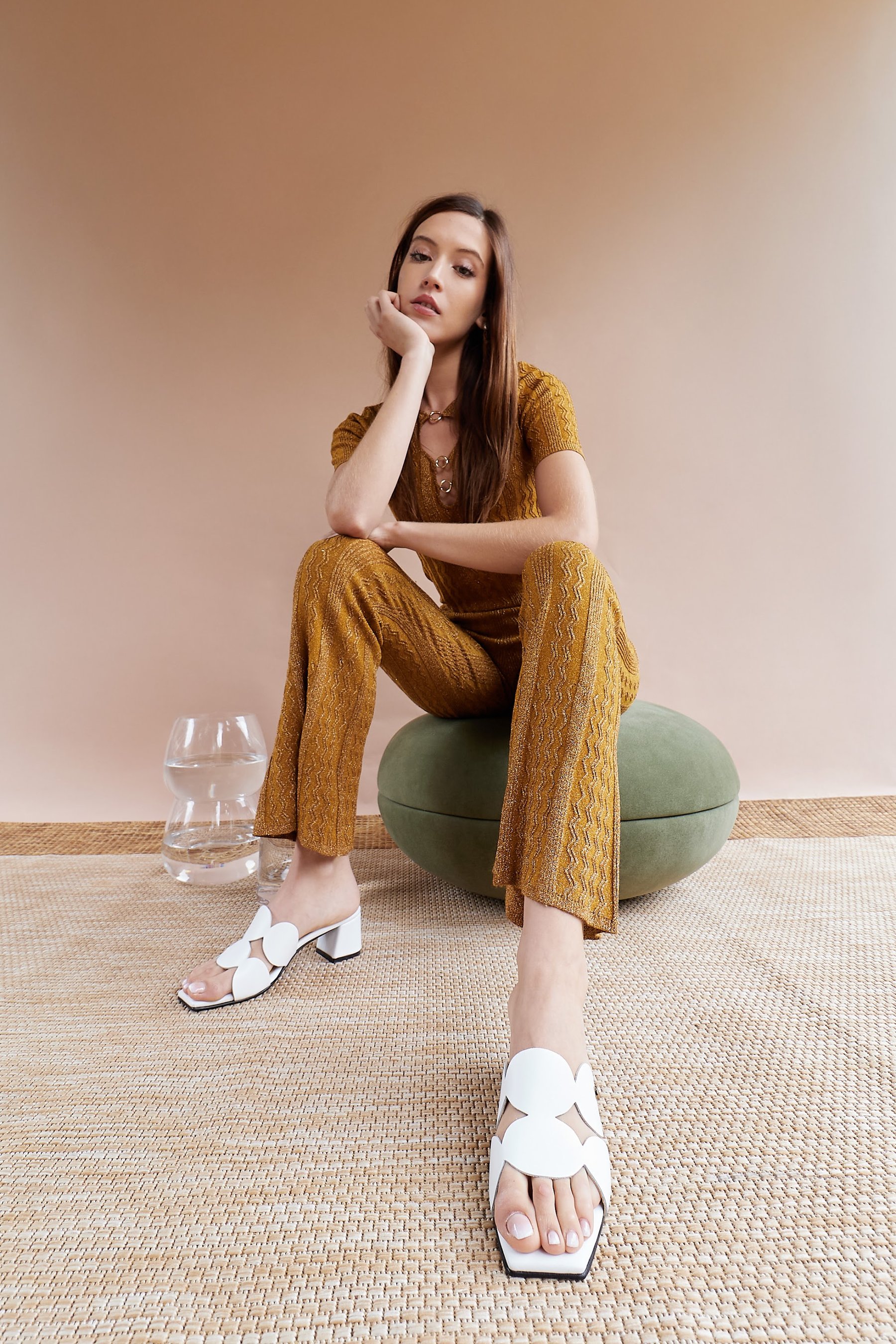 Modelo sentada en el pouf con conjunto mostaza y mule blanca.
