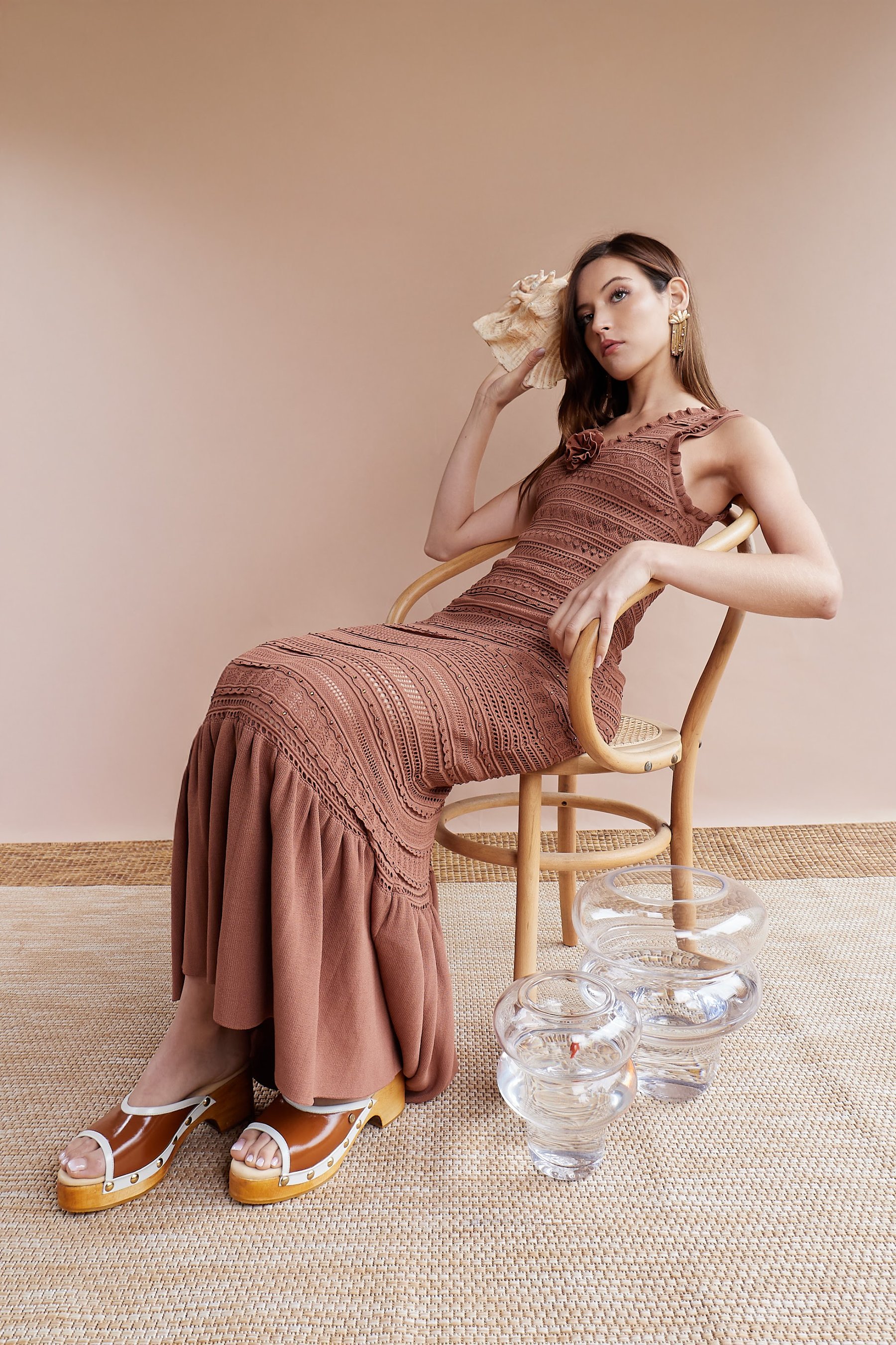 Modelo en silla con vestido plisado terracota y sandalia de tacón.